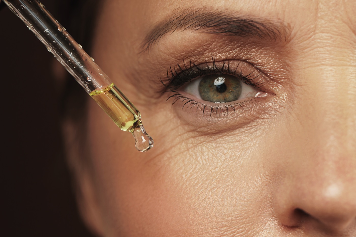 Close up photo of woman's eye using a pipette of product.