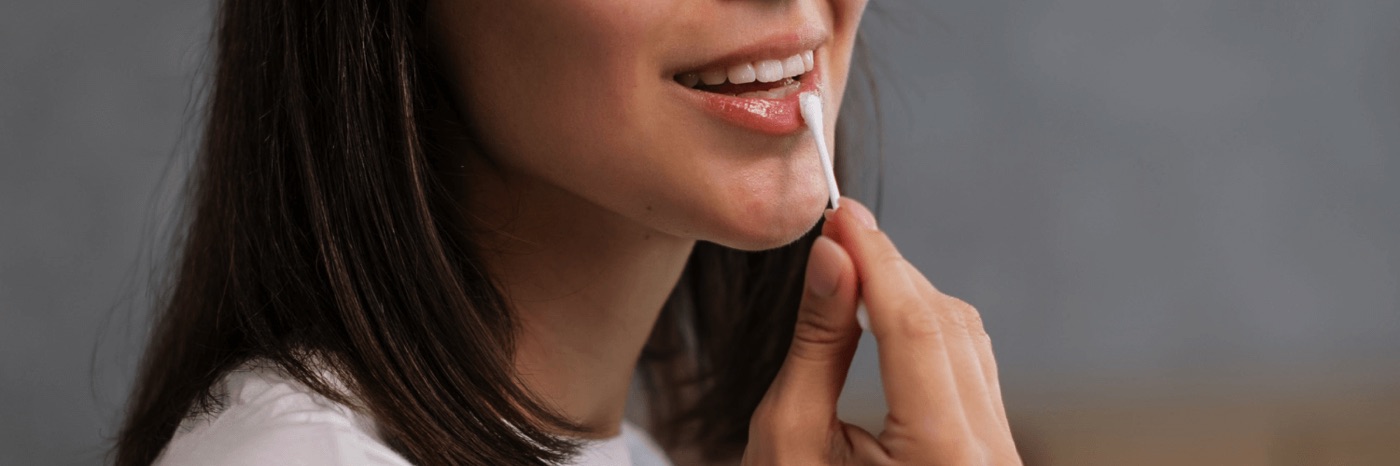Close up photo of a woman applying Oat Cosmetics lip treatment to her lips.