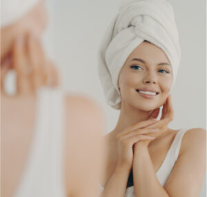A happy woman with a hair towel applying Aurafirm P to her face.