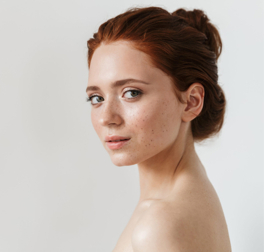 Photo of a woman with red hair looking over her shoulder at the camera with shiny skin after using Oat Lipid E.