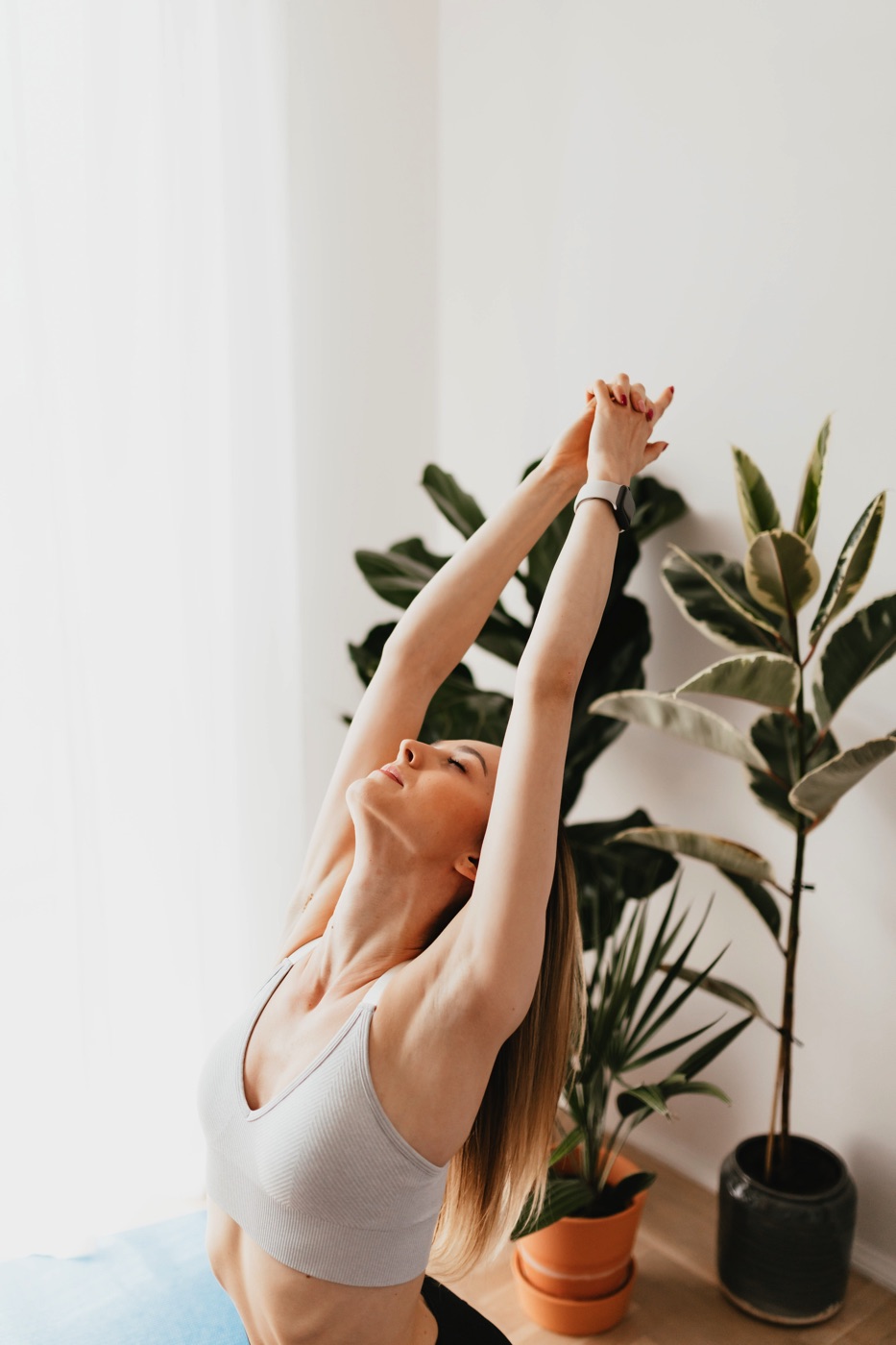 Photo of a person doing yoga stretches in their house, in front of two plants.
